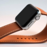 Close-up of an Apple Watch with a smooth, tan faux leather band gracefully arched, showcasing its elegant stitching, premium finish, and modern design against a soft gradient background.